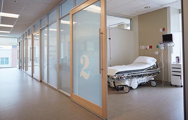 Krankenhausflur mit Blick durch geöffnete Tür in Patientenzimmer mit Patientenbiett